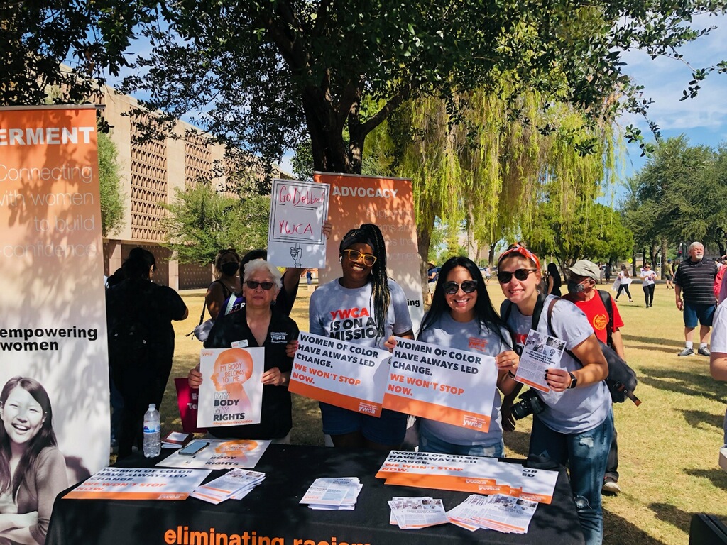 Staff stand with rally signs at the YWCA table at the 2021 Phoenix Women's March.